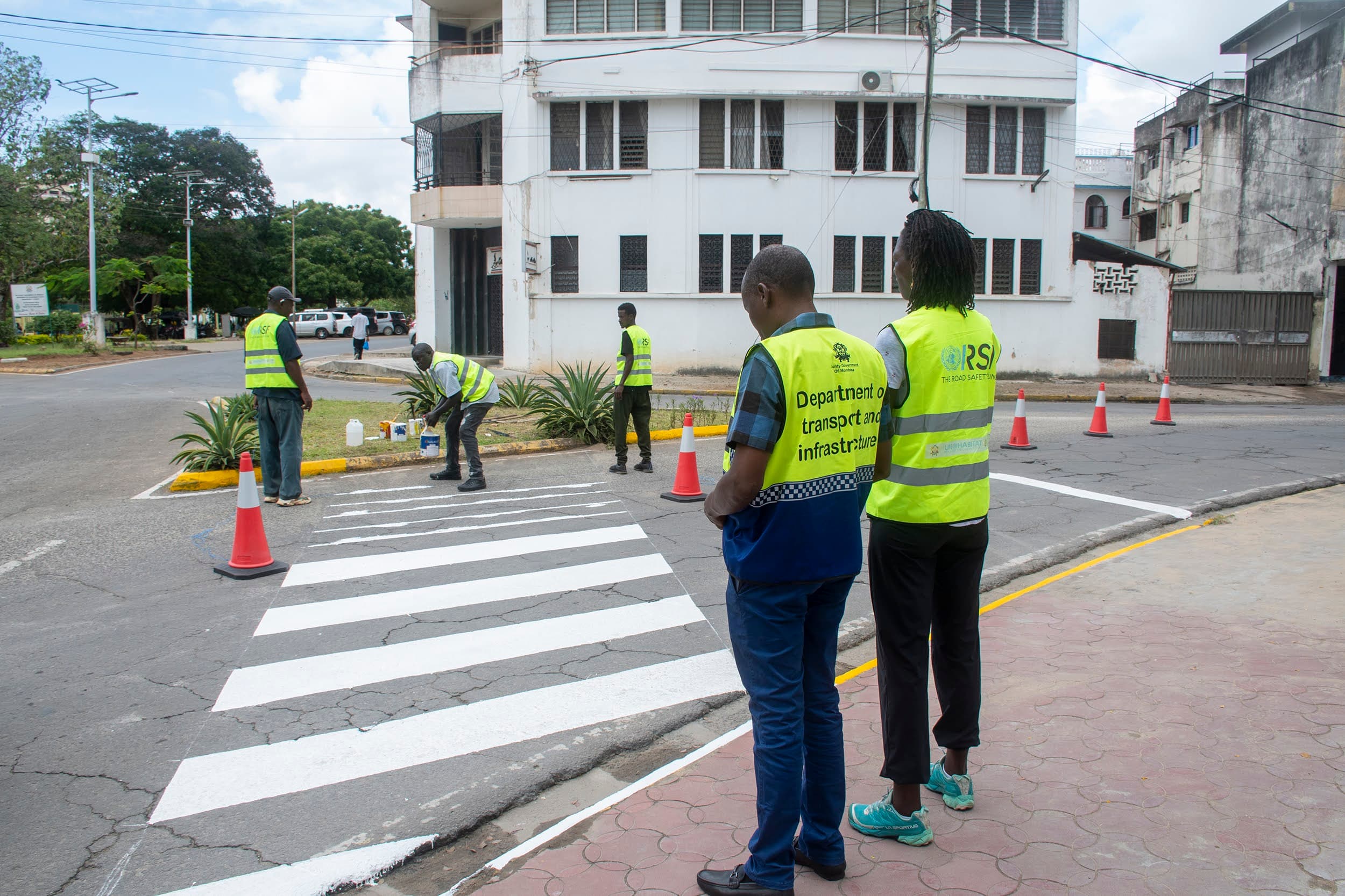 Road-safety crew in high-visibility vests marking a pedestrian crossing on an urban street